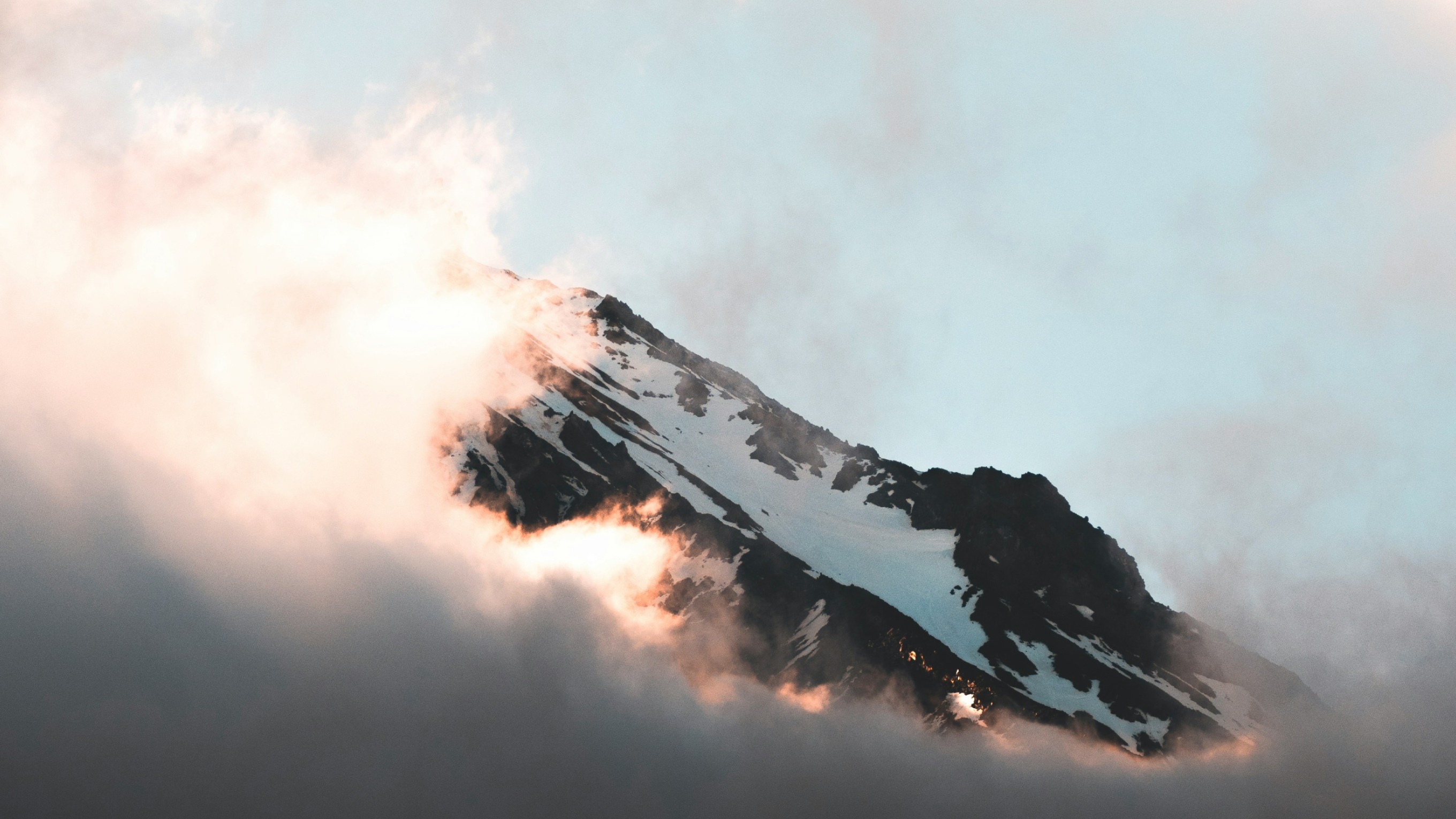 The top of a snowy mountain top with sun shining through the clouds