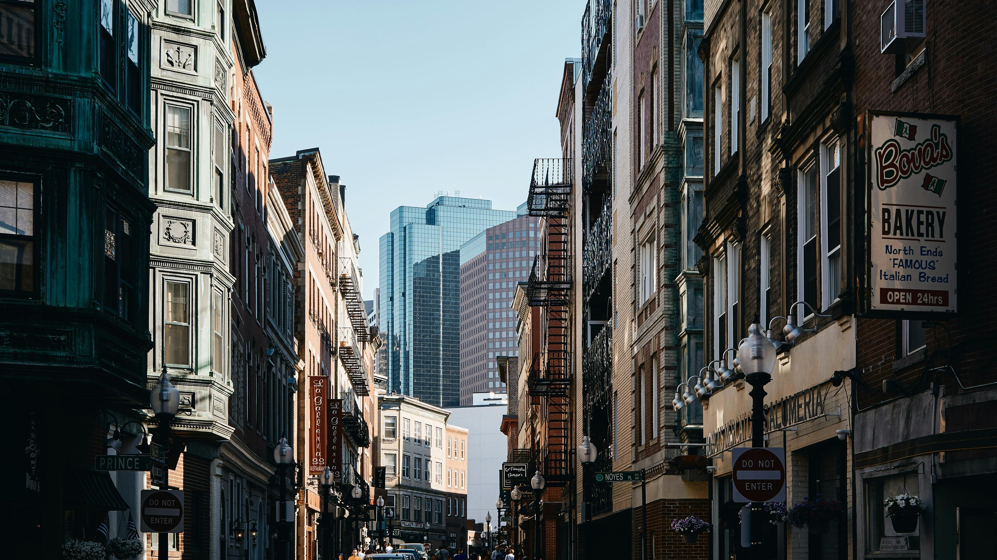 A narrow downtown Boston street of brick buildings, with Financial District towers beyond
