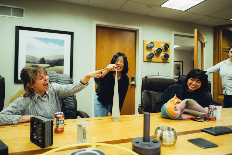 Three coworkers laugh and play with a long strip of paper around a conference table.