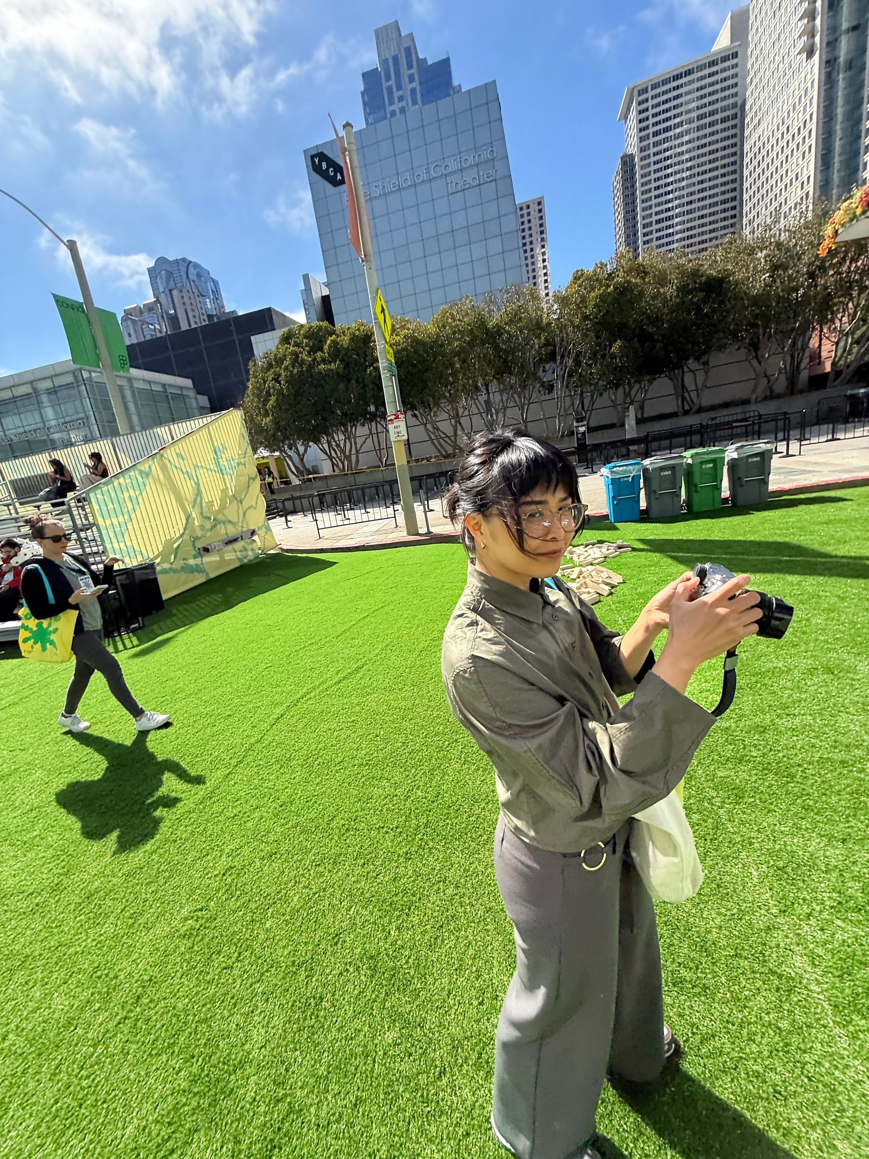 Woman holding a camera on a sunny lawn outside Yerba Buena Center for the Arts in San Francisco.
