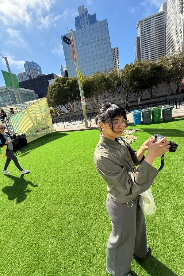 Woman holding a camera on a sunny lawn outside Yerba Buena Center for the Arts in San Francisco.
