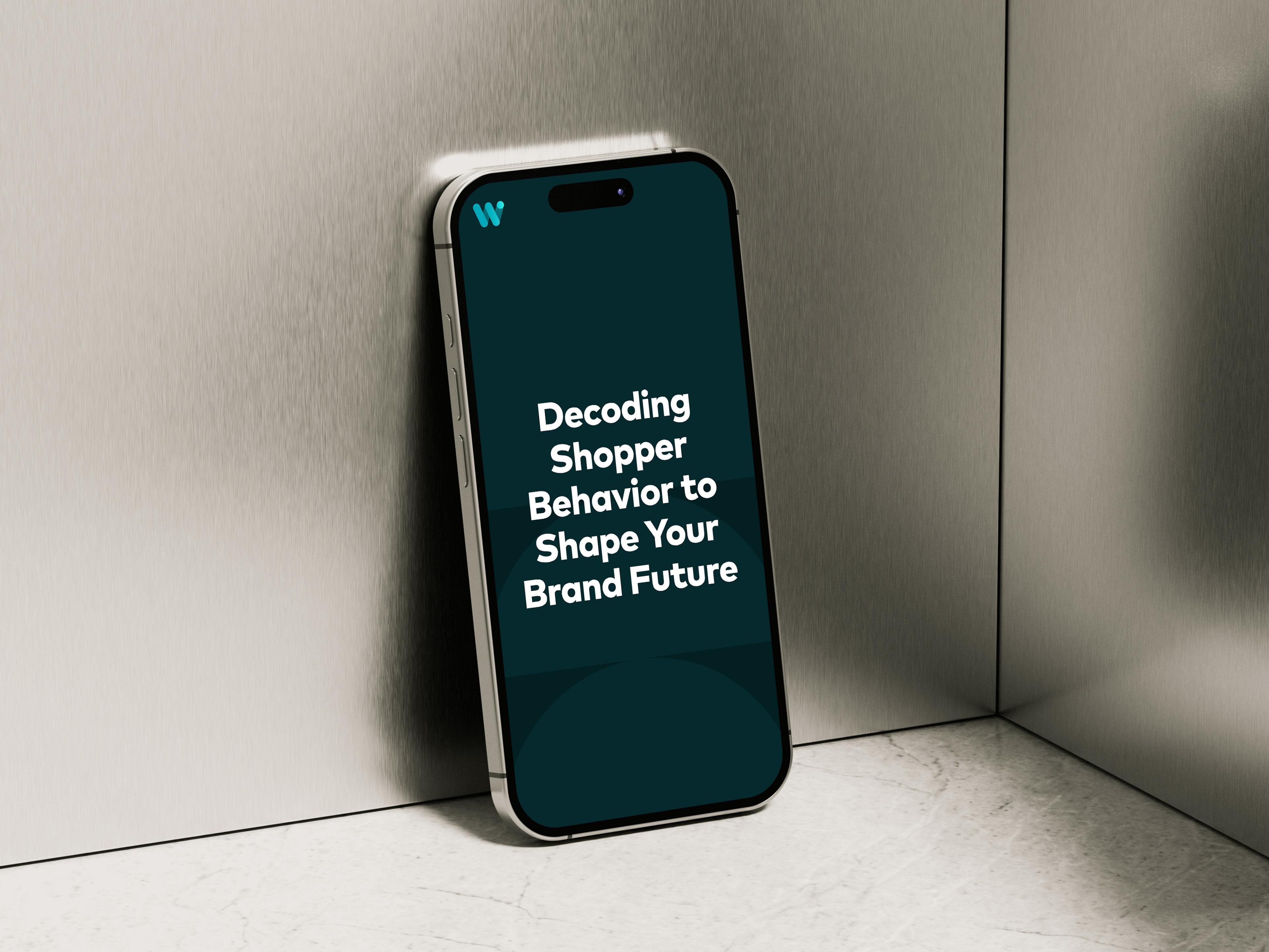 Mobile phone leaning against a brushed metal background displaying the text "Decoding Shopper Behavior to Shape Your Brand Future"