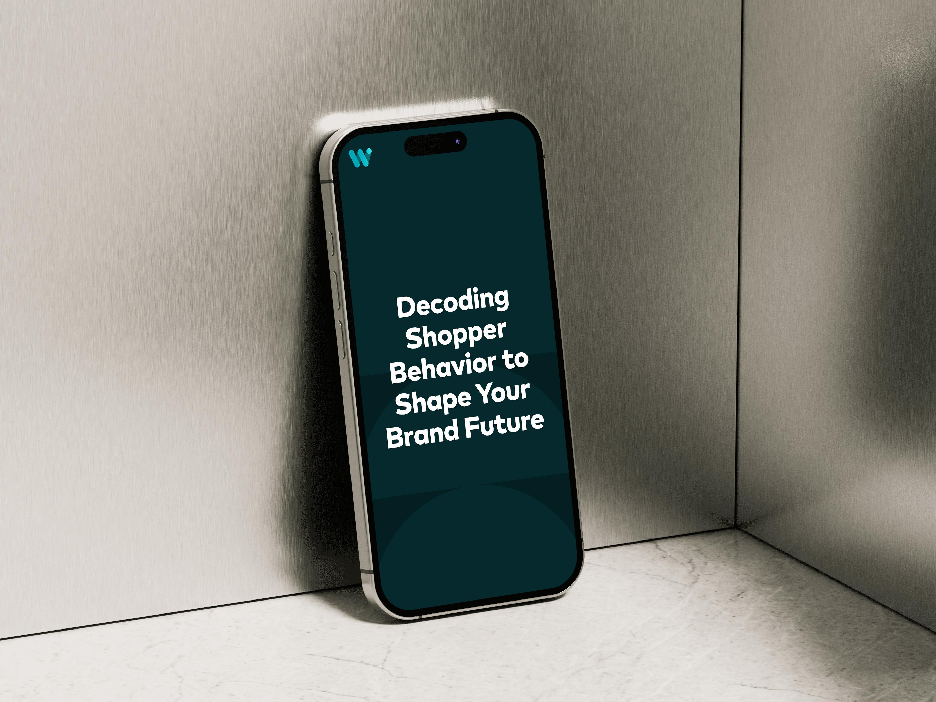 Mobile phone leaning against a brushed metal background displaying the text "Decoding Shopper Behavior to Shape Your Brand Future"
