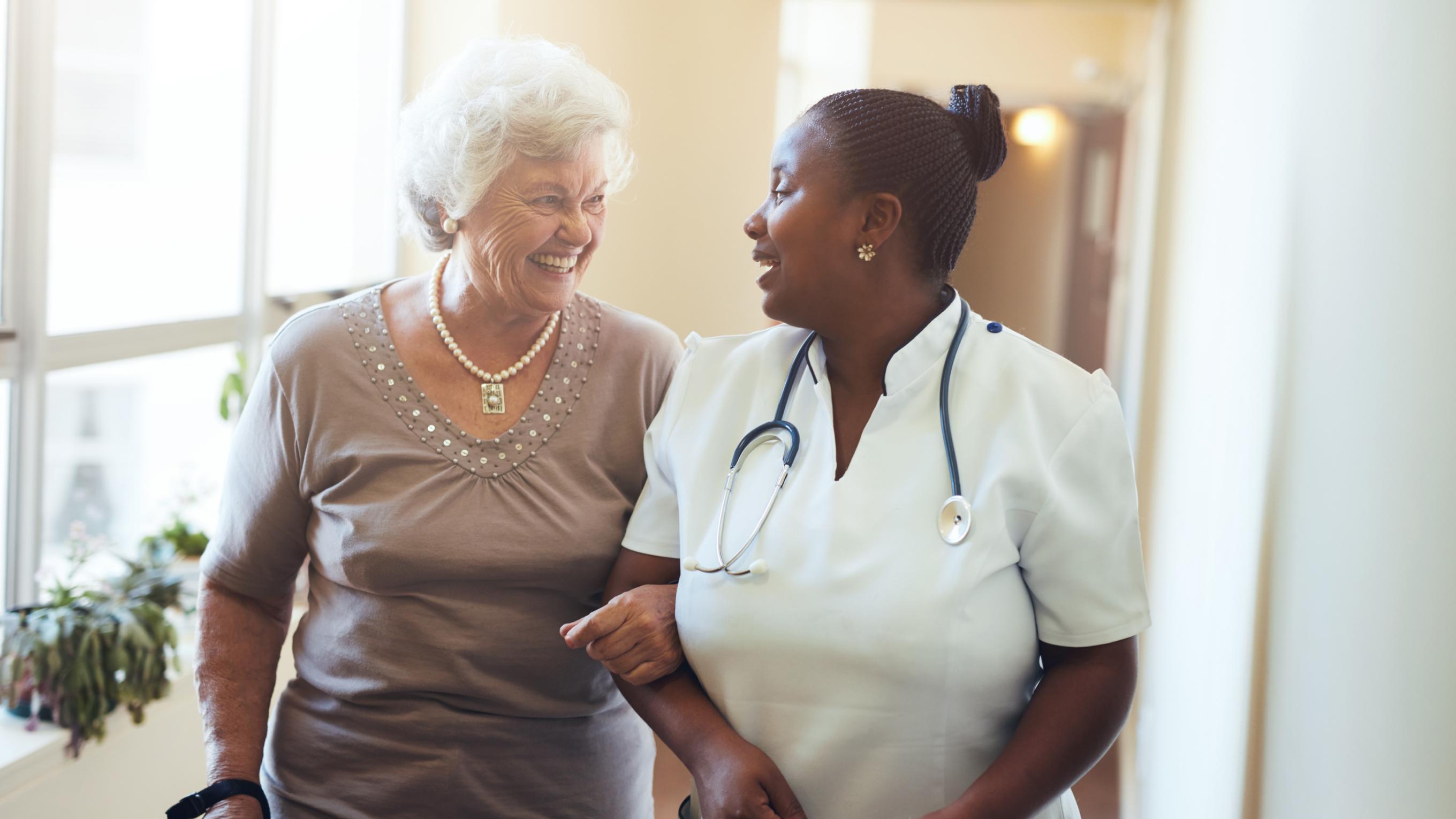 An elderly woman walking arm-in-arm with a nurse