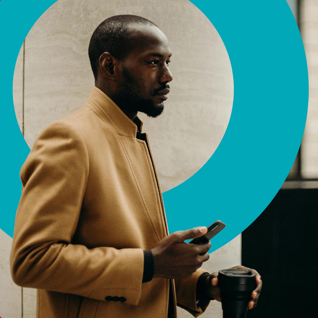 A man in a tan jacket holding a phone and a cup of coffee