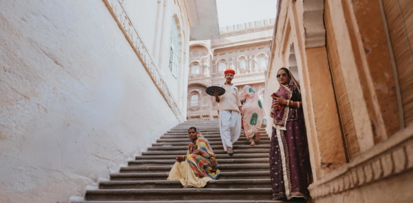 People in traditional Indian dress and contemporary sunglasses sit and stand on and old stone staircase.
