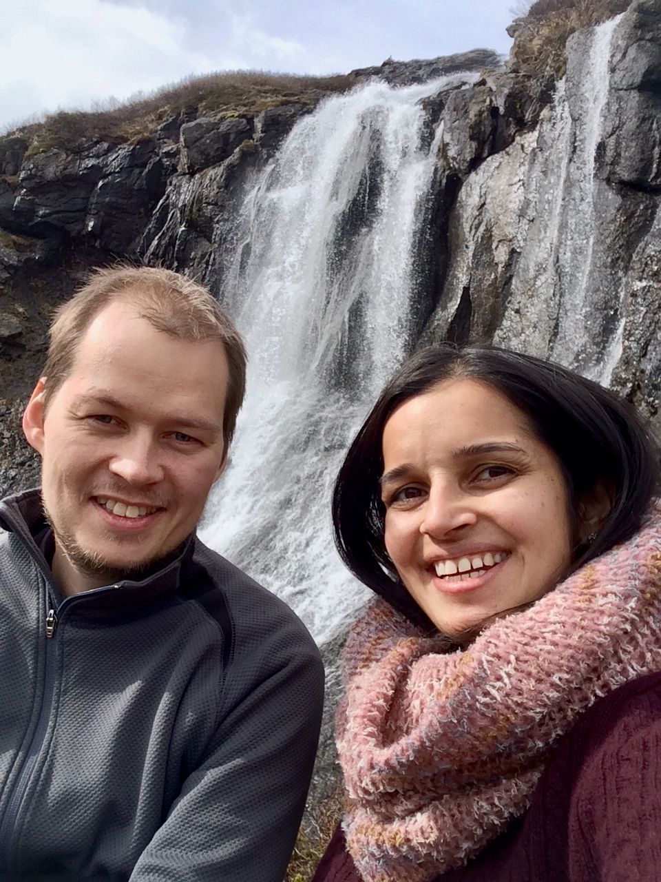 A man and a woman smile in front of a waterfall.