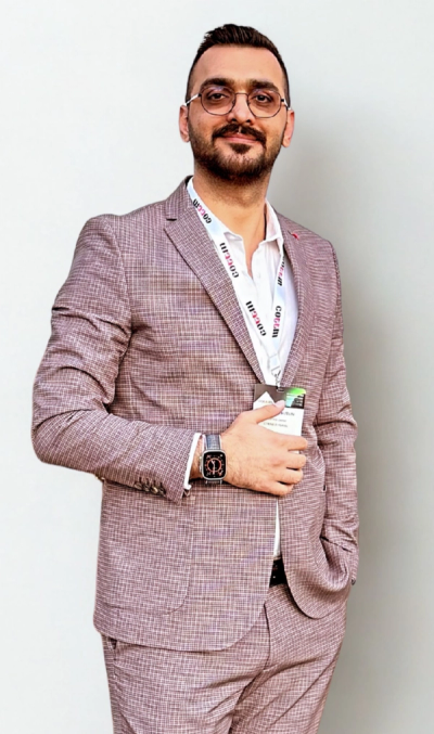 A smiling man with glasses, in a pink suit.