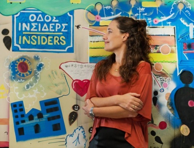 A Greek CEO with her head turned sideways and arms crossed. 