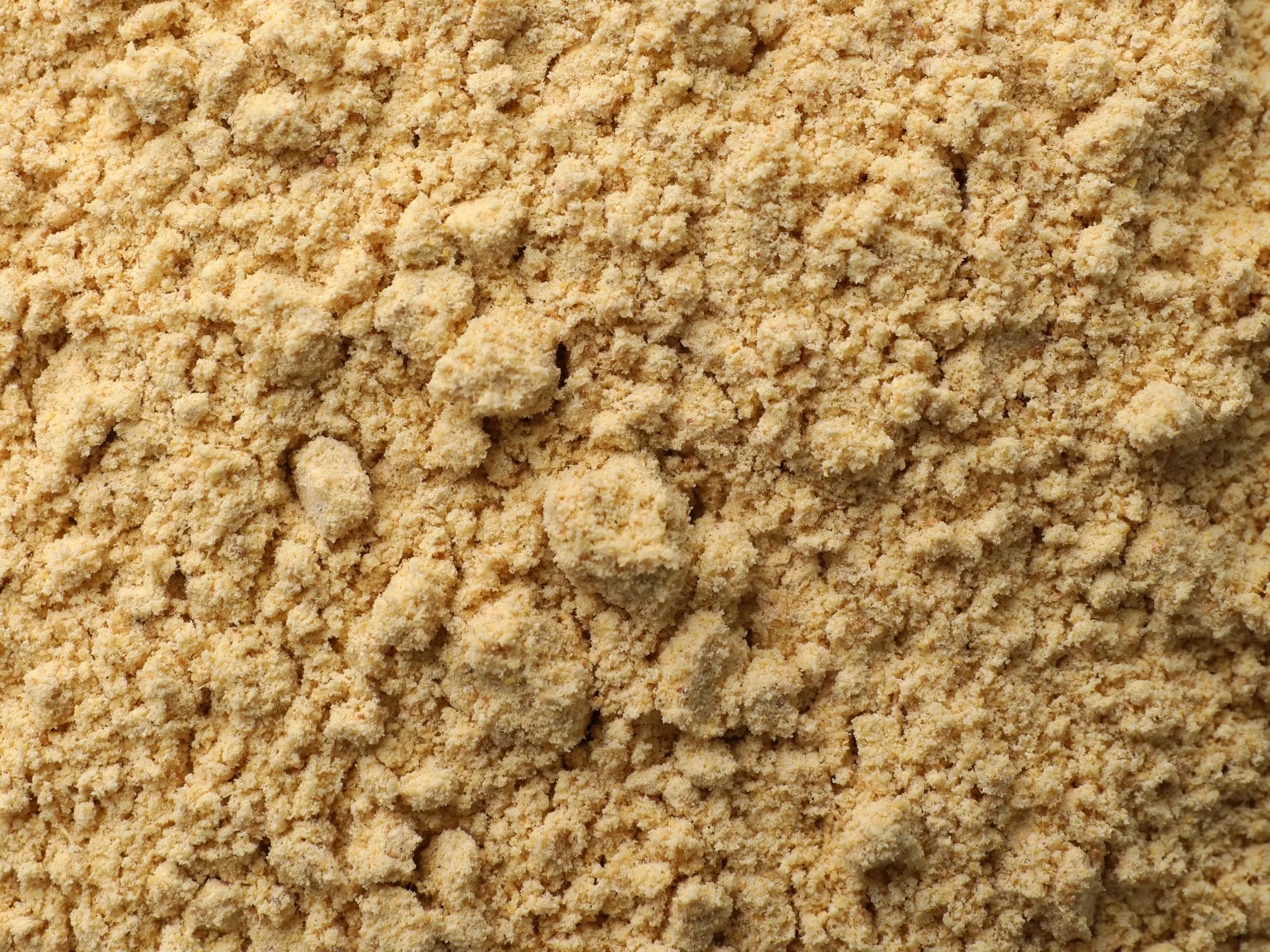 A close-up of coarse Whole Ground Yellow Mustard, showing its granular texture and rich yellow color.