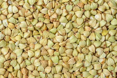 A close-up of clean, raw White Buckwheat Groats, showcasing their pale color and pyramid-like shape.