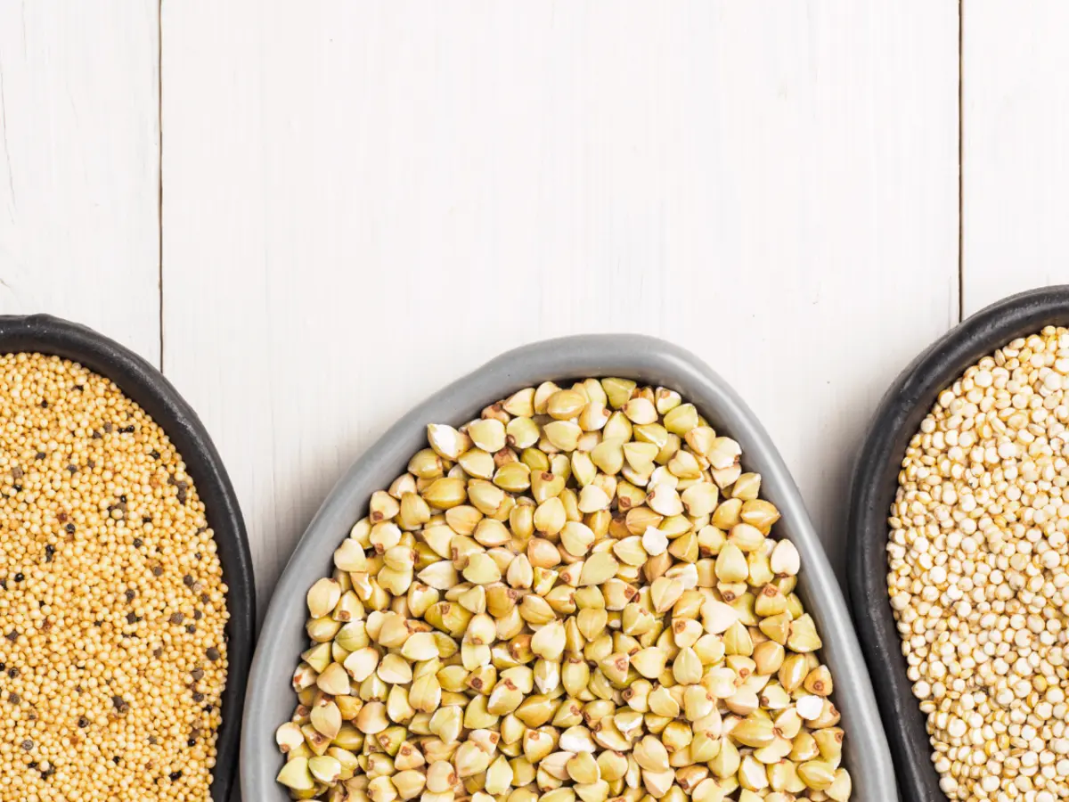 Bovenaanzicht van drie moderne kommen met een verscheidenheid aan speciale granen waaronder boekweit, quinoa en amarant op een schone witte houten ondergrond.
