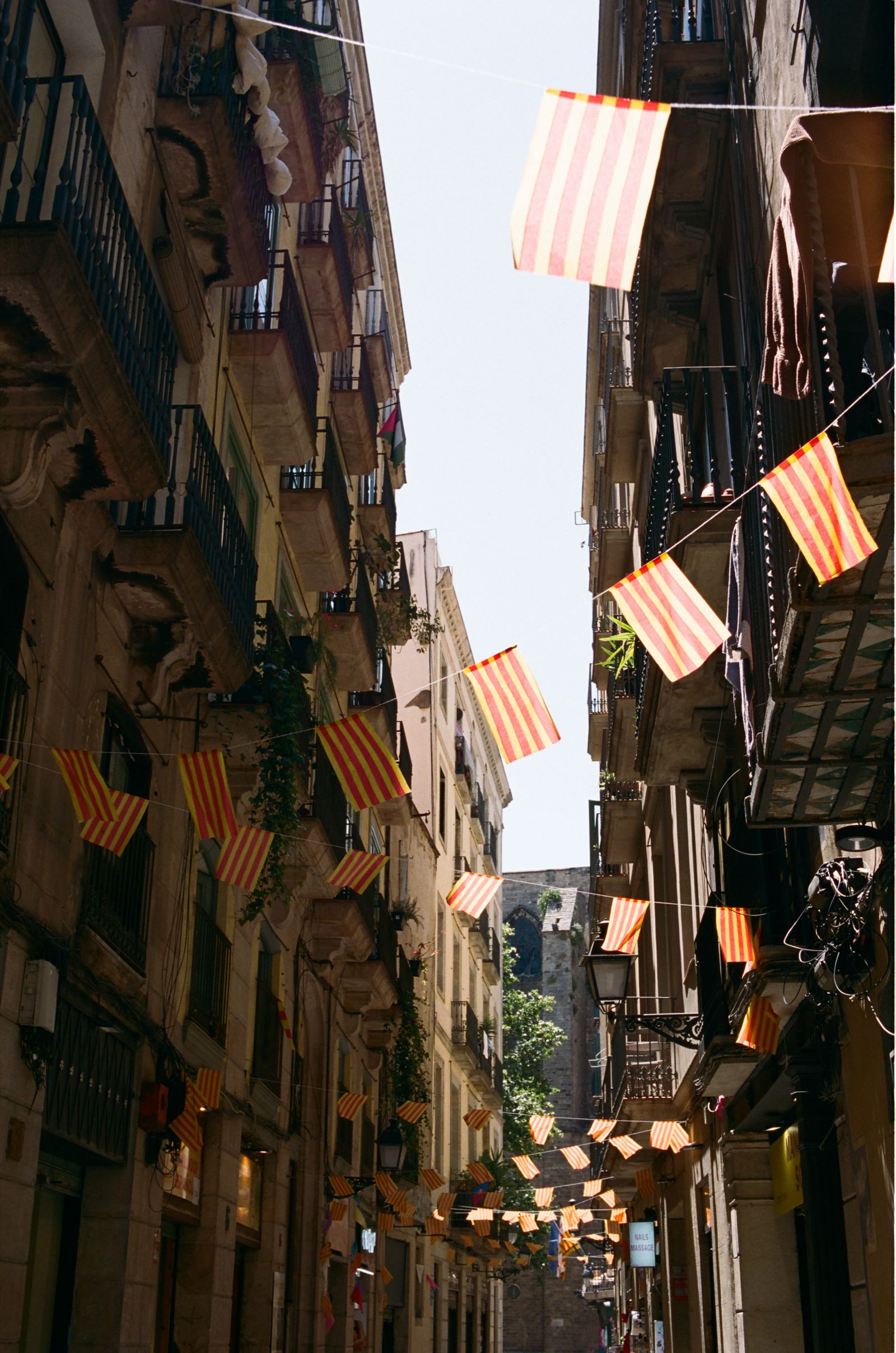Red and yellow striped Catalan flags strung between tall balconied buildings on a narrow shaded city alley.