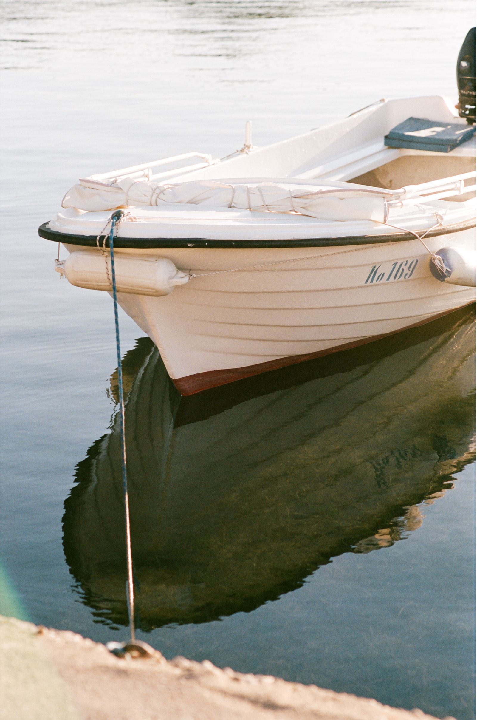 The bow of a small wooden rowboat numbered "No 169" rests on still water, its dark reflection mirrored below.