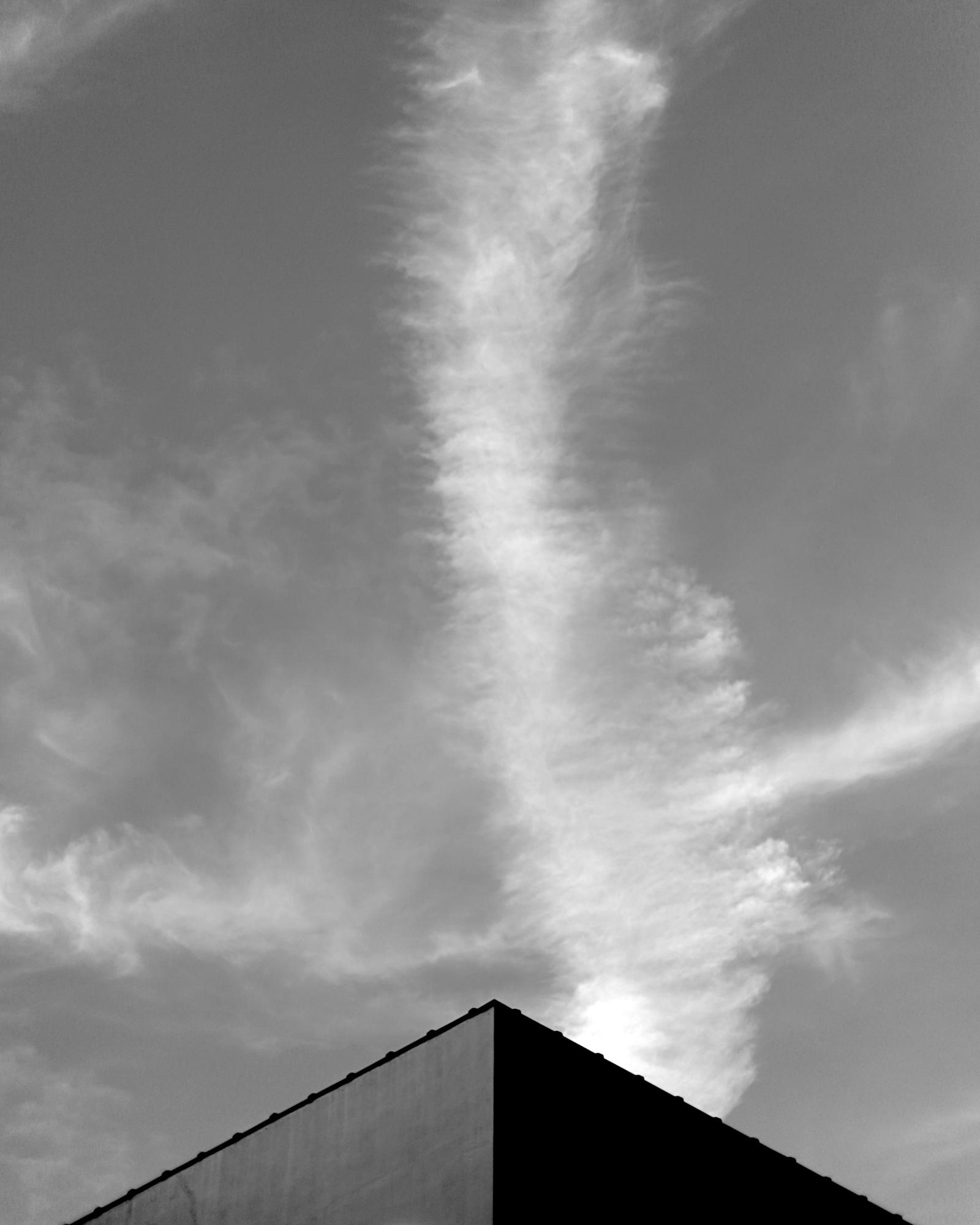 Black-and-white triangular rooftop peak of a building against a sky with a vertical streak of cloud.