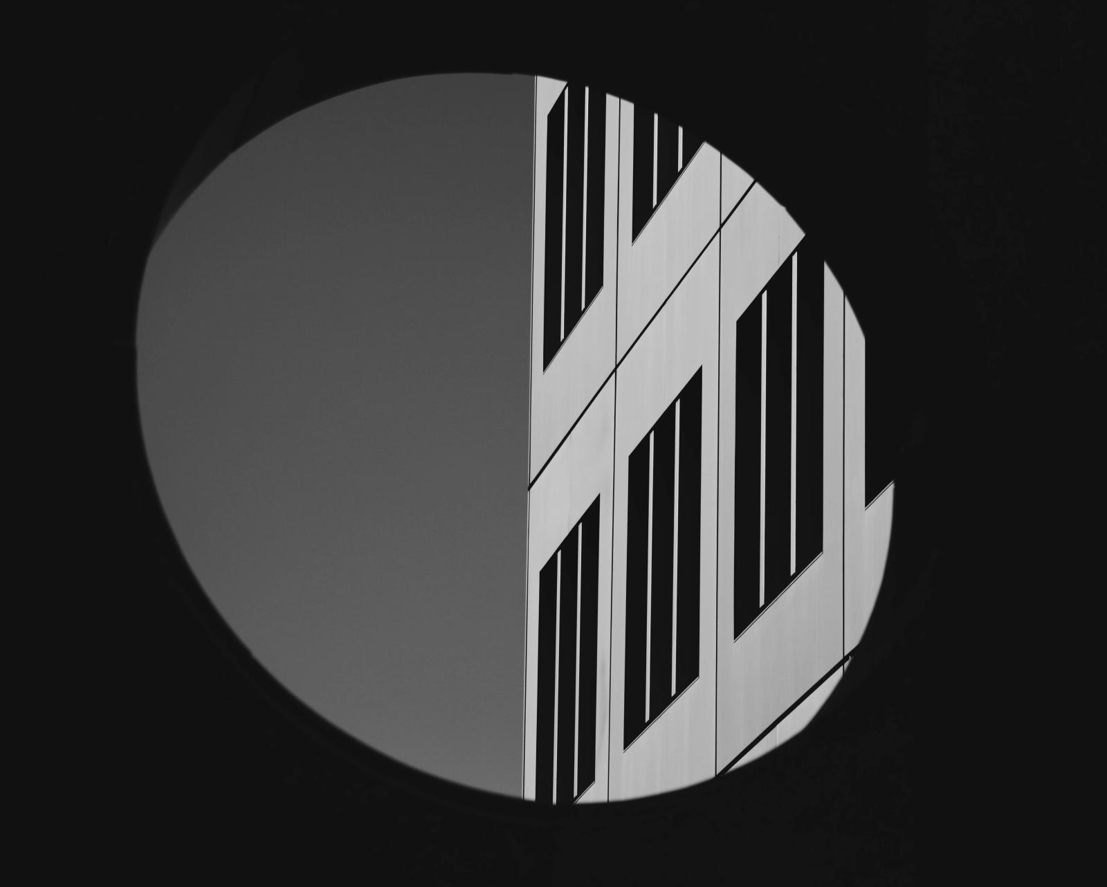 Black-and-white circular vignette framing the diagonal striped facade of a building against open sky.