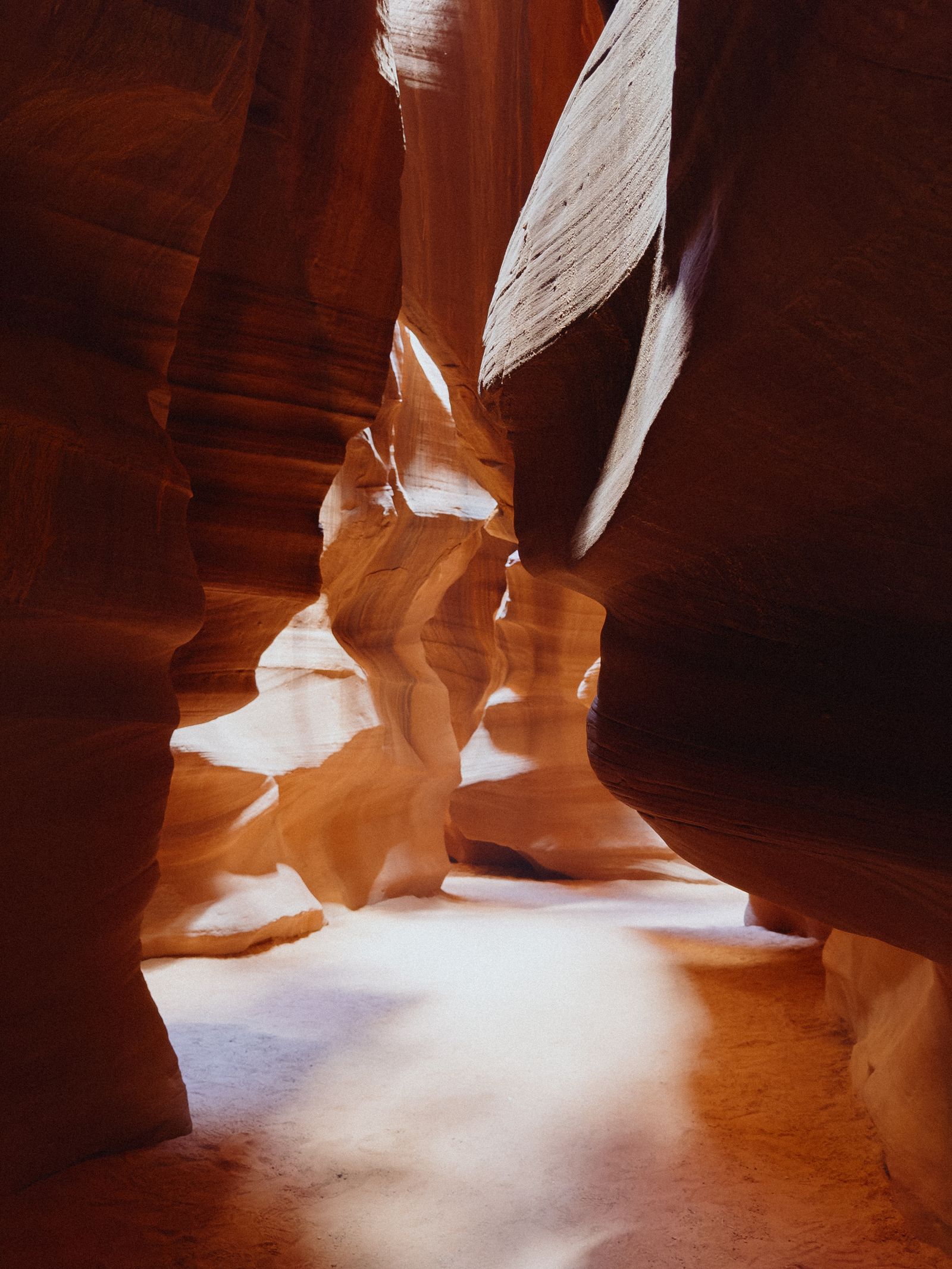 Sunlight filters into a narrow, curving sandstone slot canyon, illuminating the smooth banded rock walls.