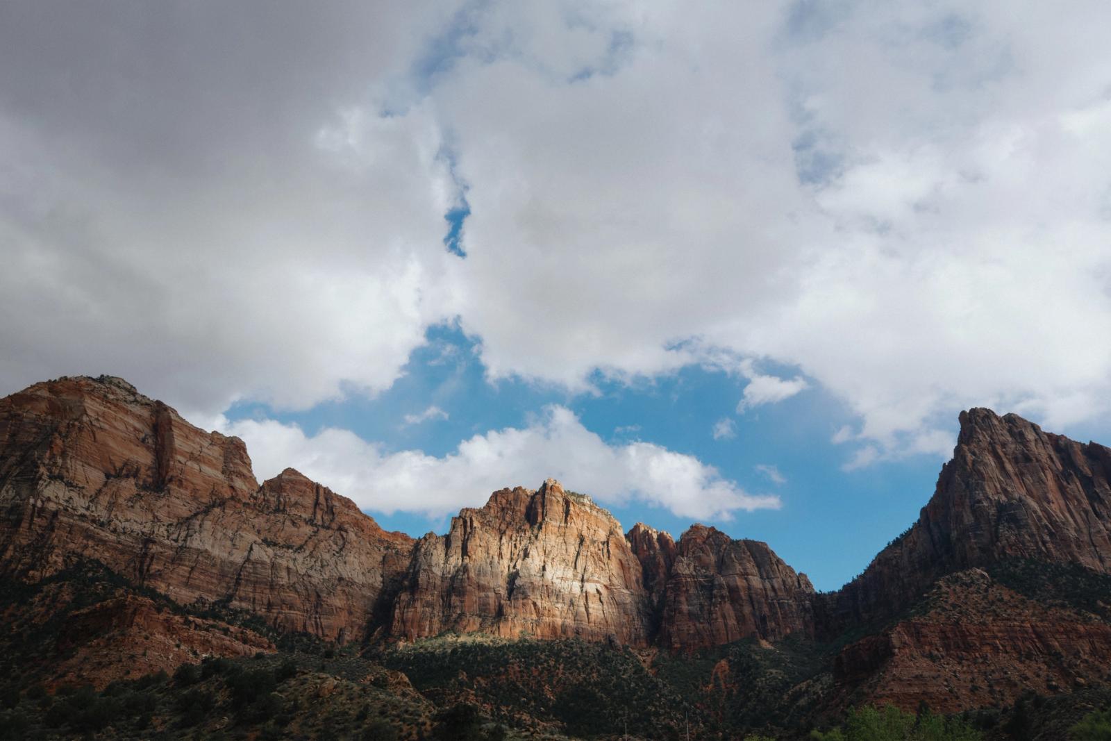 Jagged red-rock desert peaks rise beneath a dramatic sky of storm clouds breaking to reveal patches of blue.