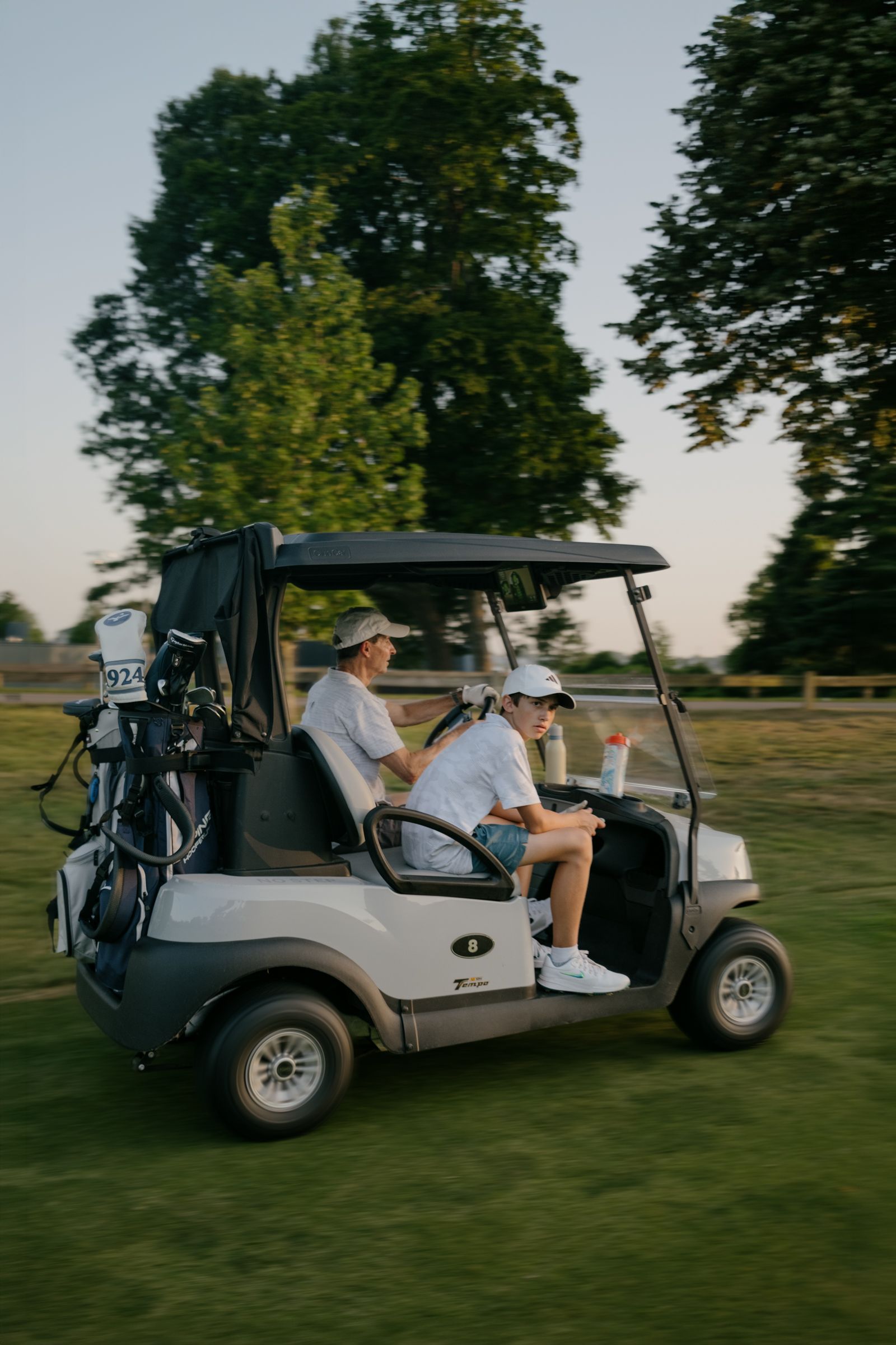 Boy and man ride in golf cart at golden hour. 