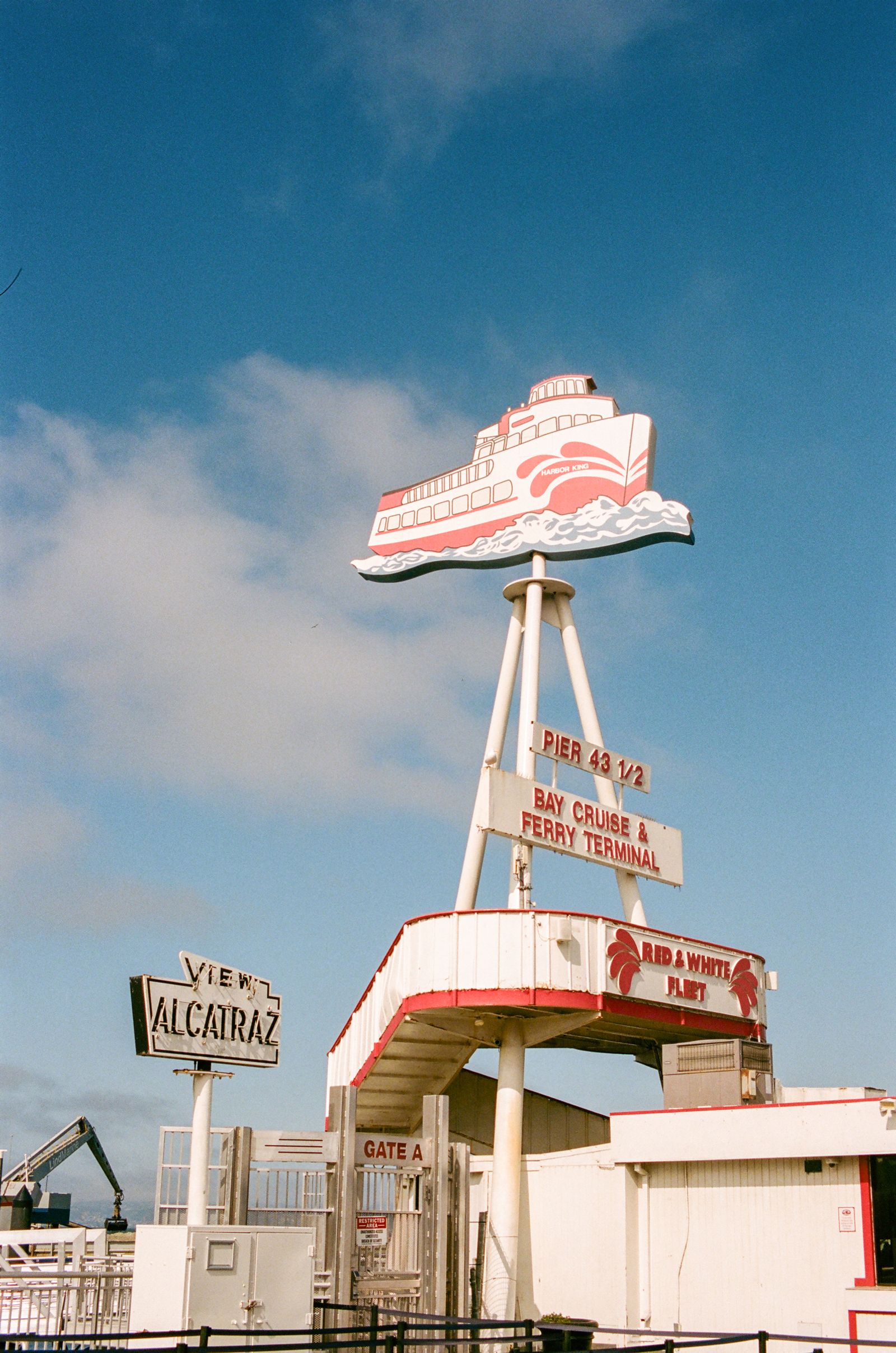 The red-and-white Pier 43½ ferry terminal sign, topped by a cut-out paddle steamer, stands against a blue sky beside a smaller sign reading “View Alcatraz”.