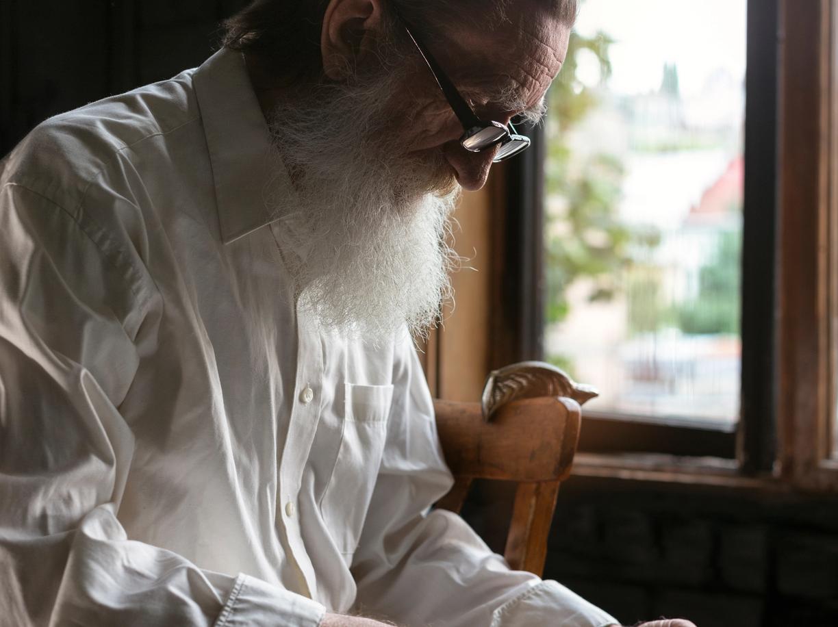 Elderly bearded man reading scripture by a sunlit window