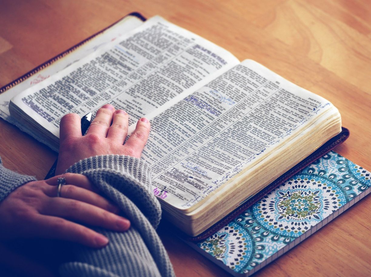 Open Bible resting on a wooden table beside a patterned cover