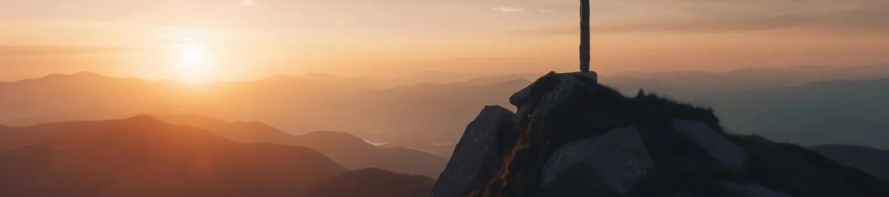 Cross silhouetted against a mountain sunset