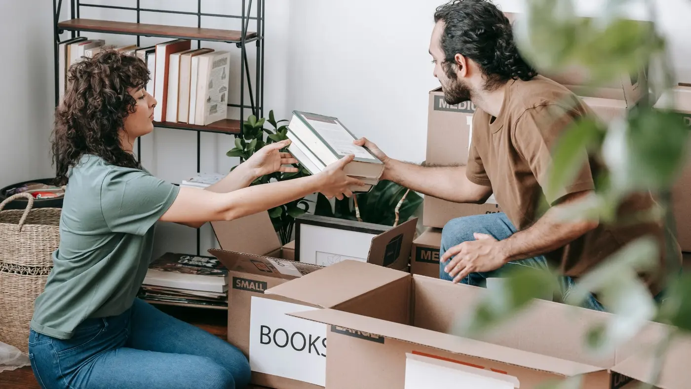 A couple sorting books and packing household belongings into moving boxes.