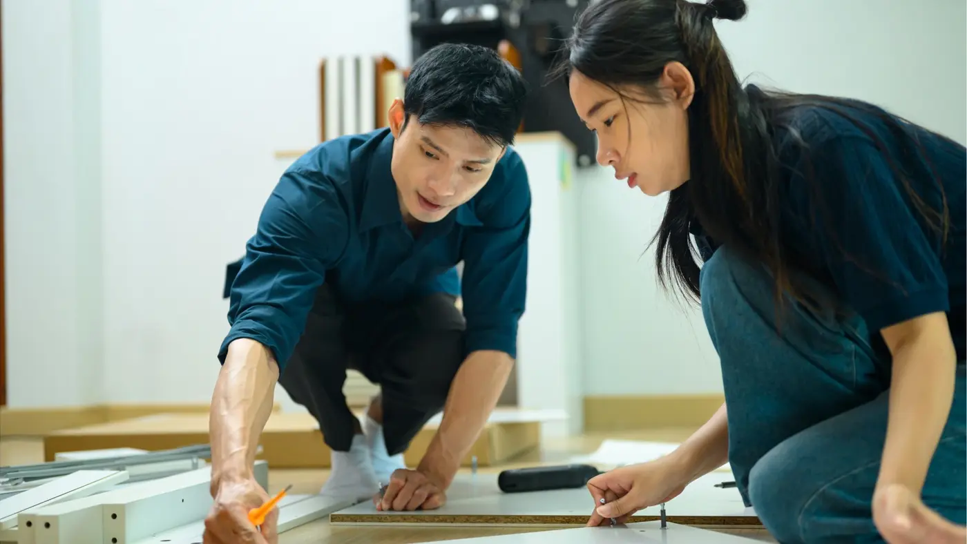 Two people assembling furniture together using tools and wooden panels.