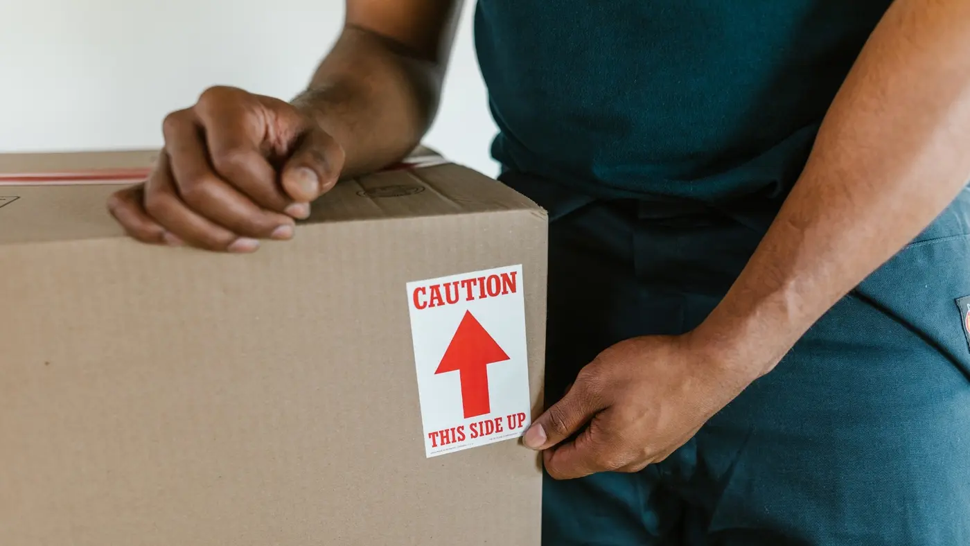A moving professional applying a “This Side Up” label to a cardboard box.