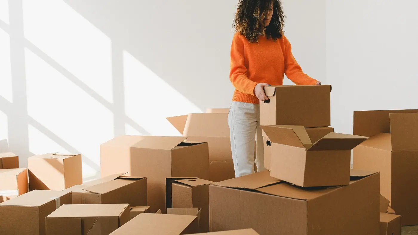 A woman placing a cardboard box on top of other moving boxes while preparing to move.