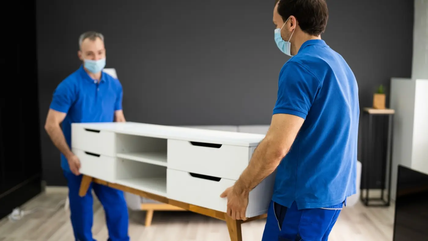 Movers carefully carrying a white cabinet during a home relocation.