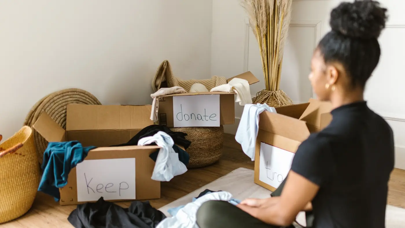 A woman sorting clothes and household items into boxes labelled “Keep” and “Donate.”