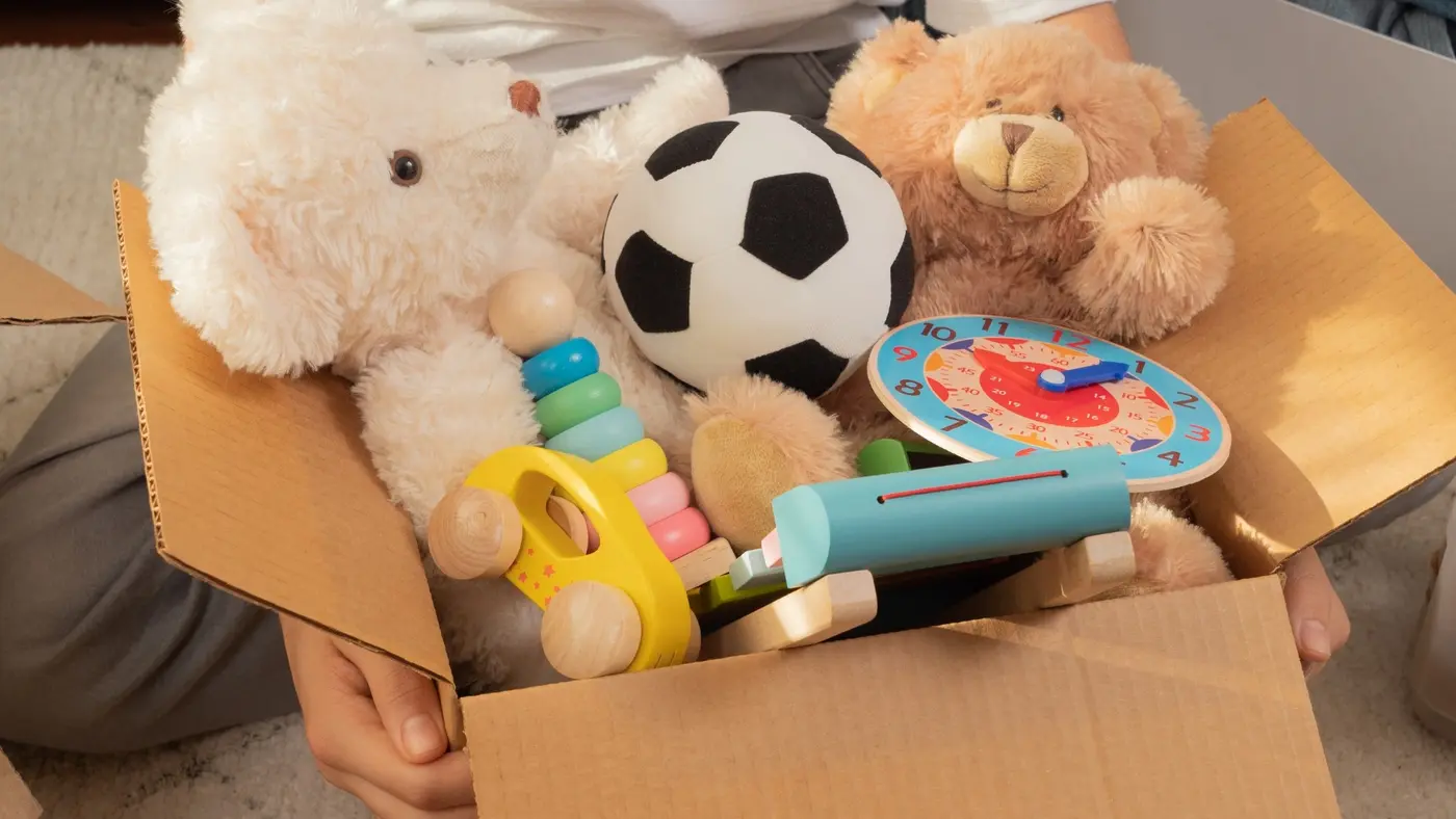 2. Image 2: Teddy bears, toys, and a ball packed inside a cardboard box for moving.