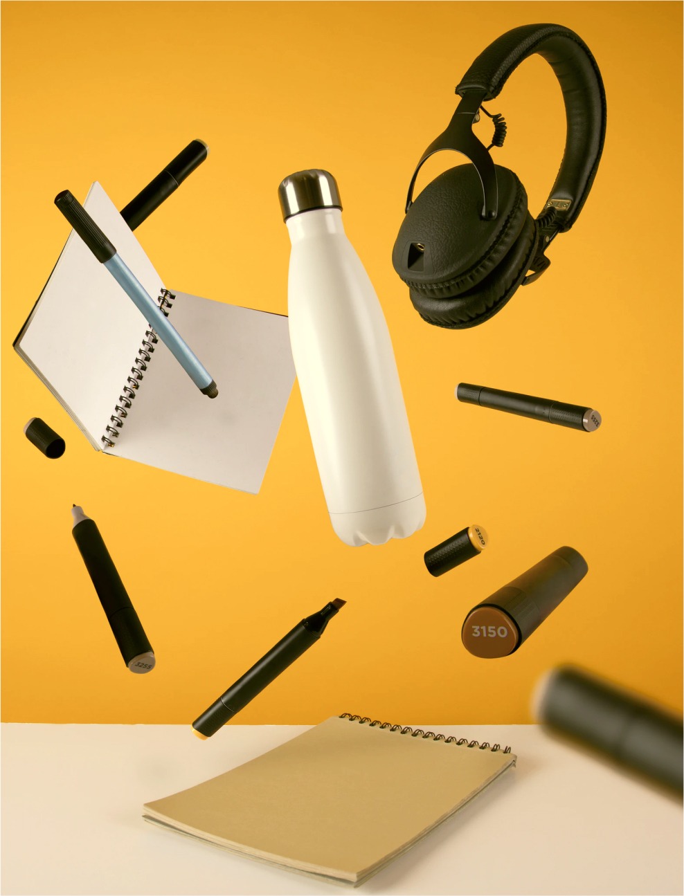 Penner, flasker og headset flyr i lufa – med en sterk gul bakgrunn. 