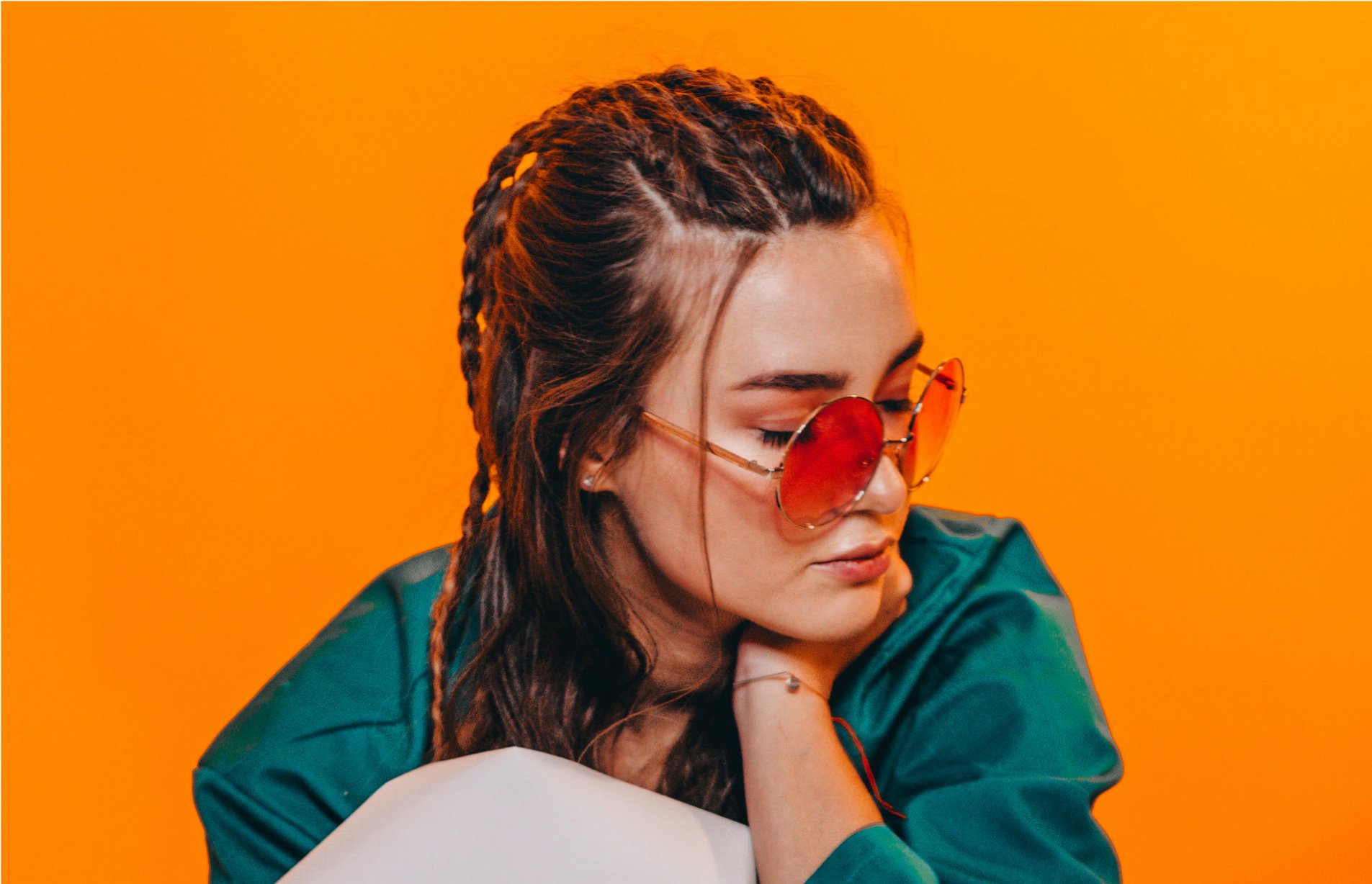 Kul jente med solbriller og flettet frisyre. Knall oransje bakgrunn. Foto