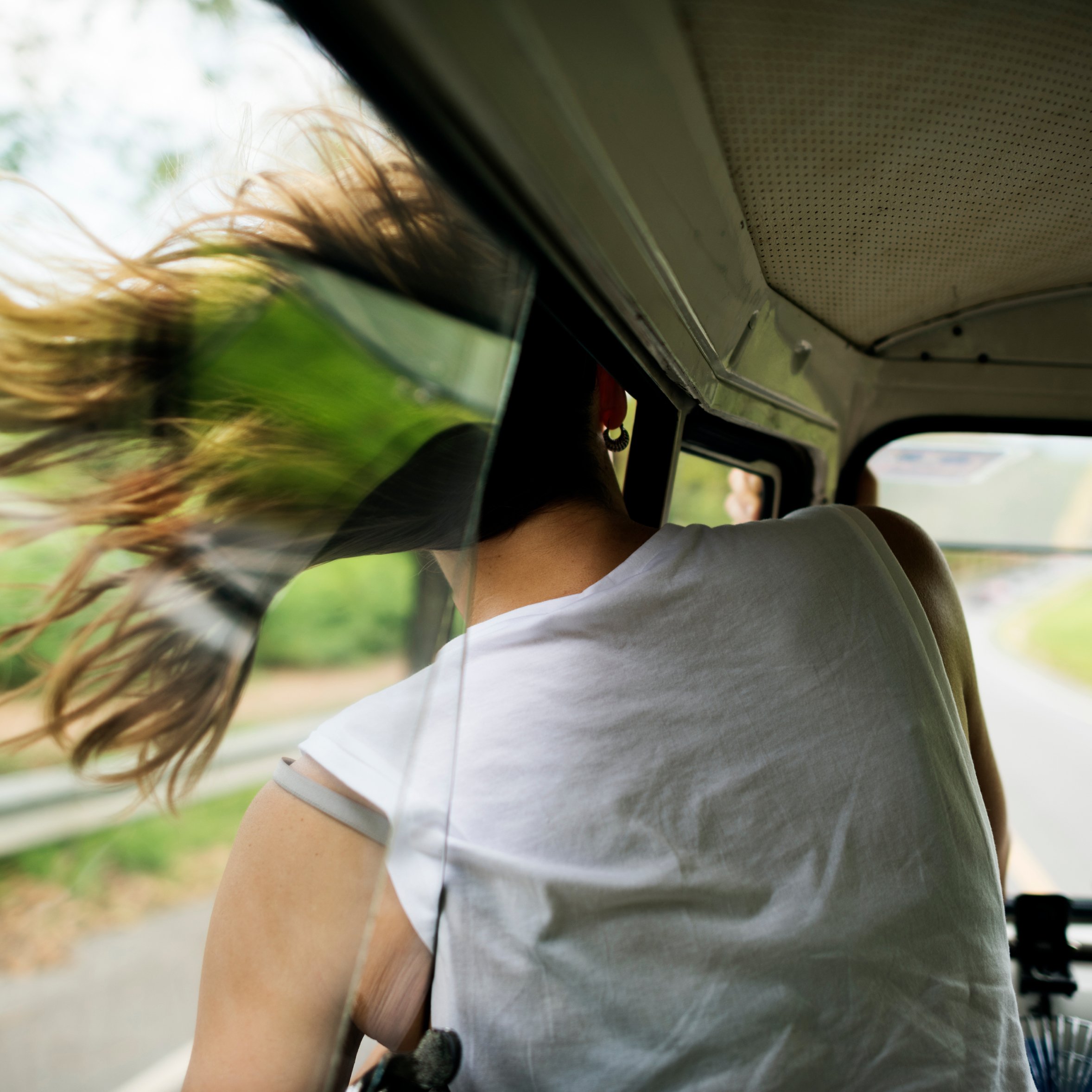 Dame har hodet ut av bilvinduet i fart, håret blåser i vinden. Foto