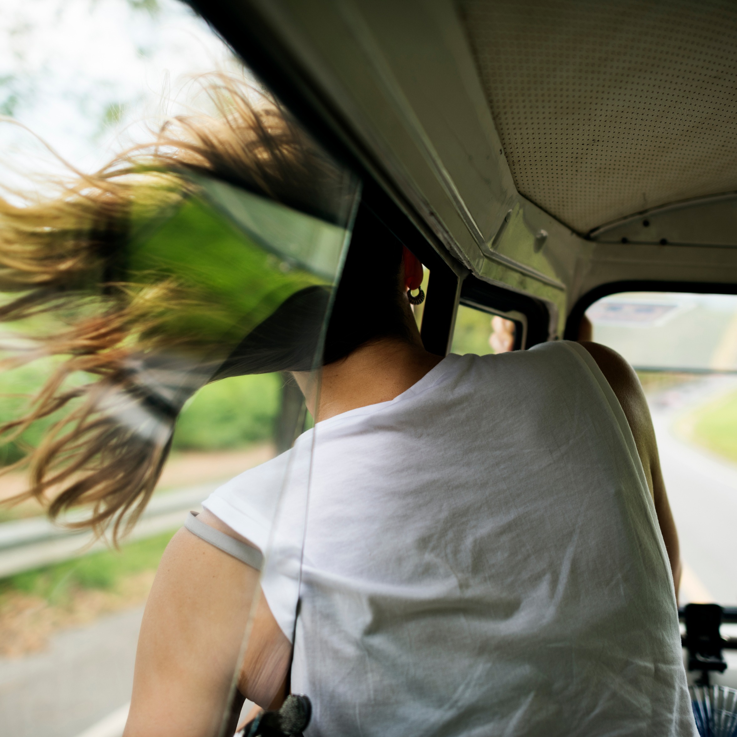 Dame har hodet ut av bilvinduet i fart, håret blåser i vinden. Foto