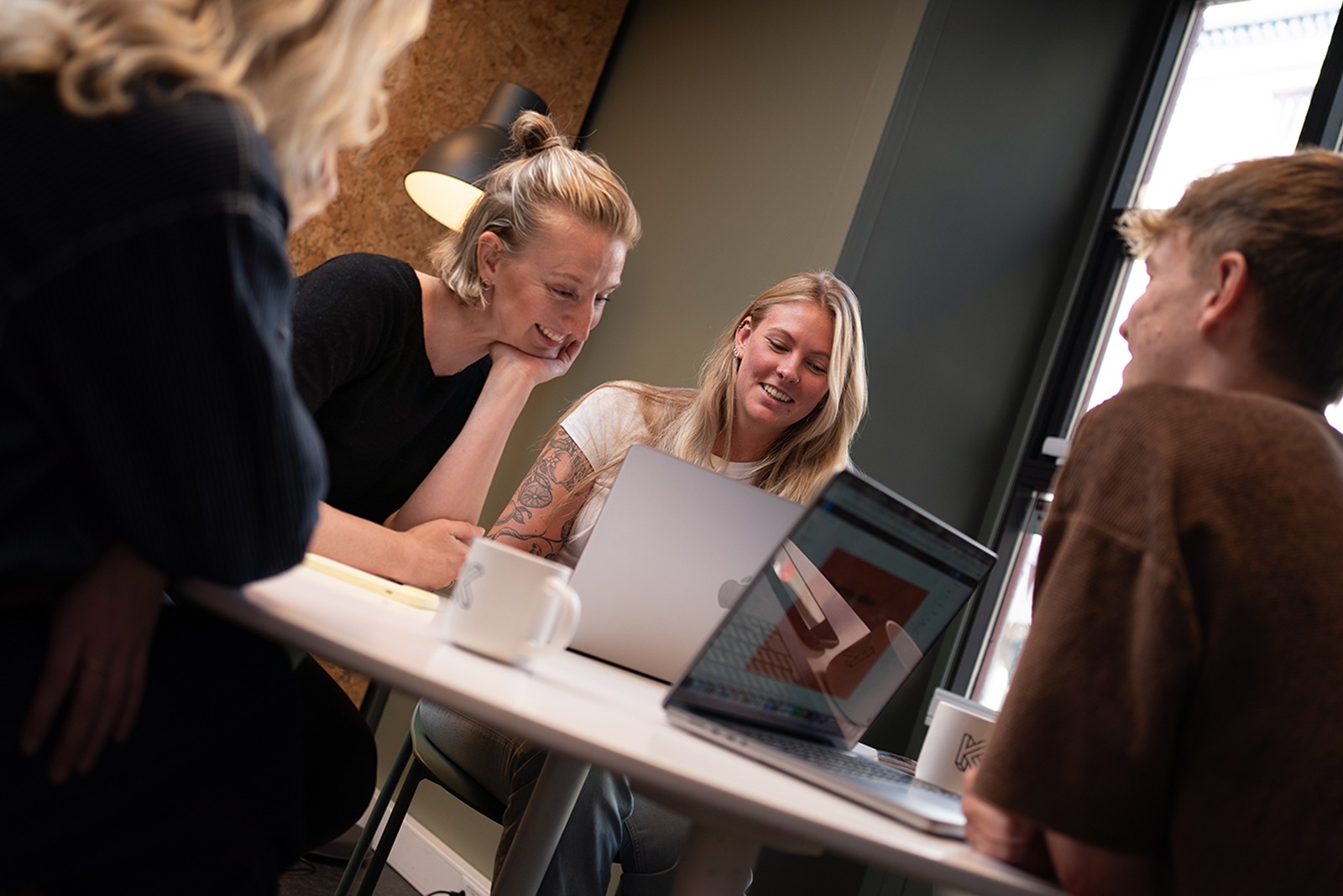 Fire i teamet sitter på et bord, ser på en mac. 