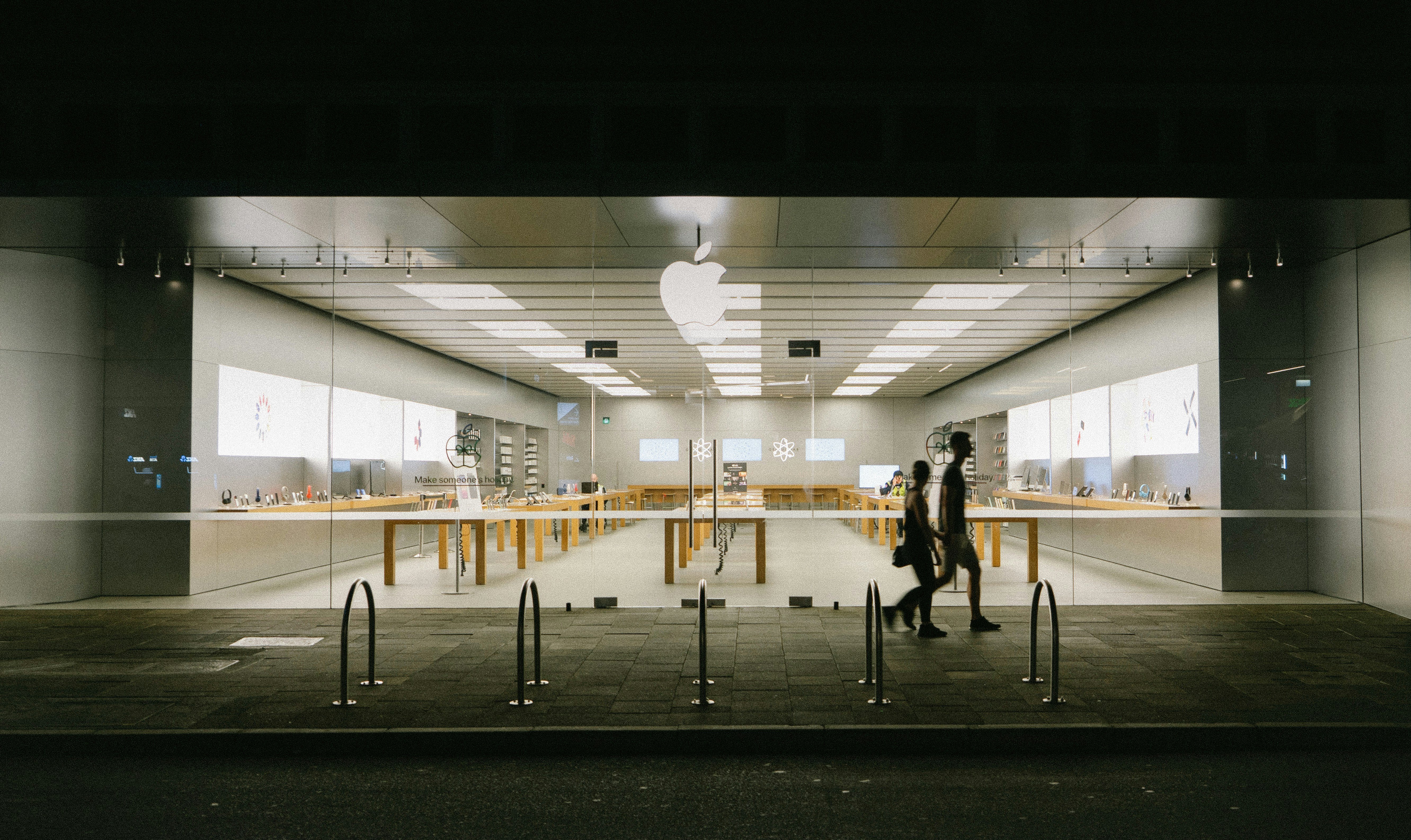 Uten i en Apple Store, der vi ser en glassvegg inn til trebordene med produktene. Foto.