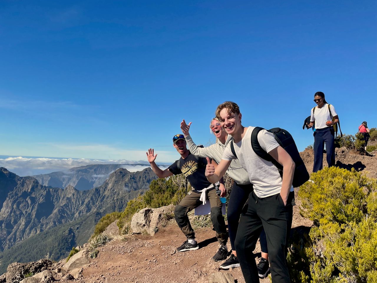 Fire i temaet står på et fjell i madeira, to vinker til kameraet på en humoristisk måte, en av de gir en thumbs opp og smiler