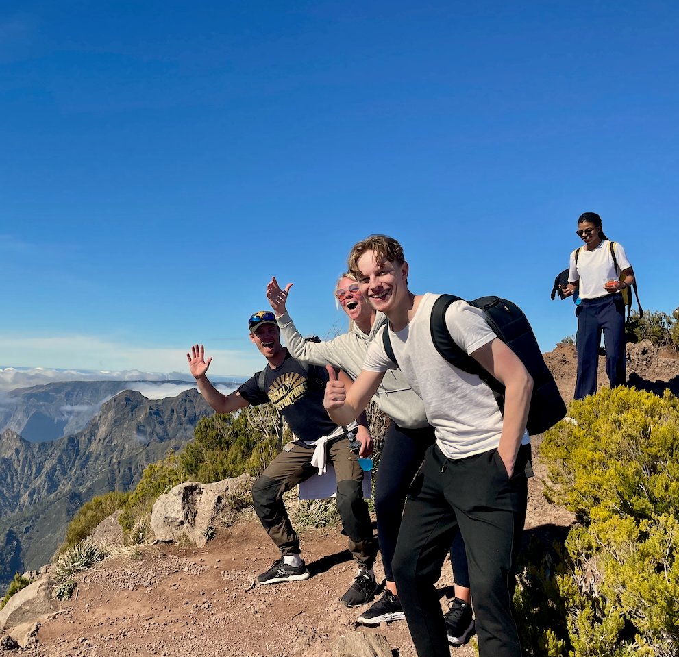 Fire i temaet står på et fjell i madeira, to vinker til kameraet på en humoristisk måte, en av de gir en thumbs opp og smiler