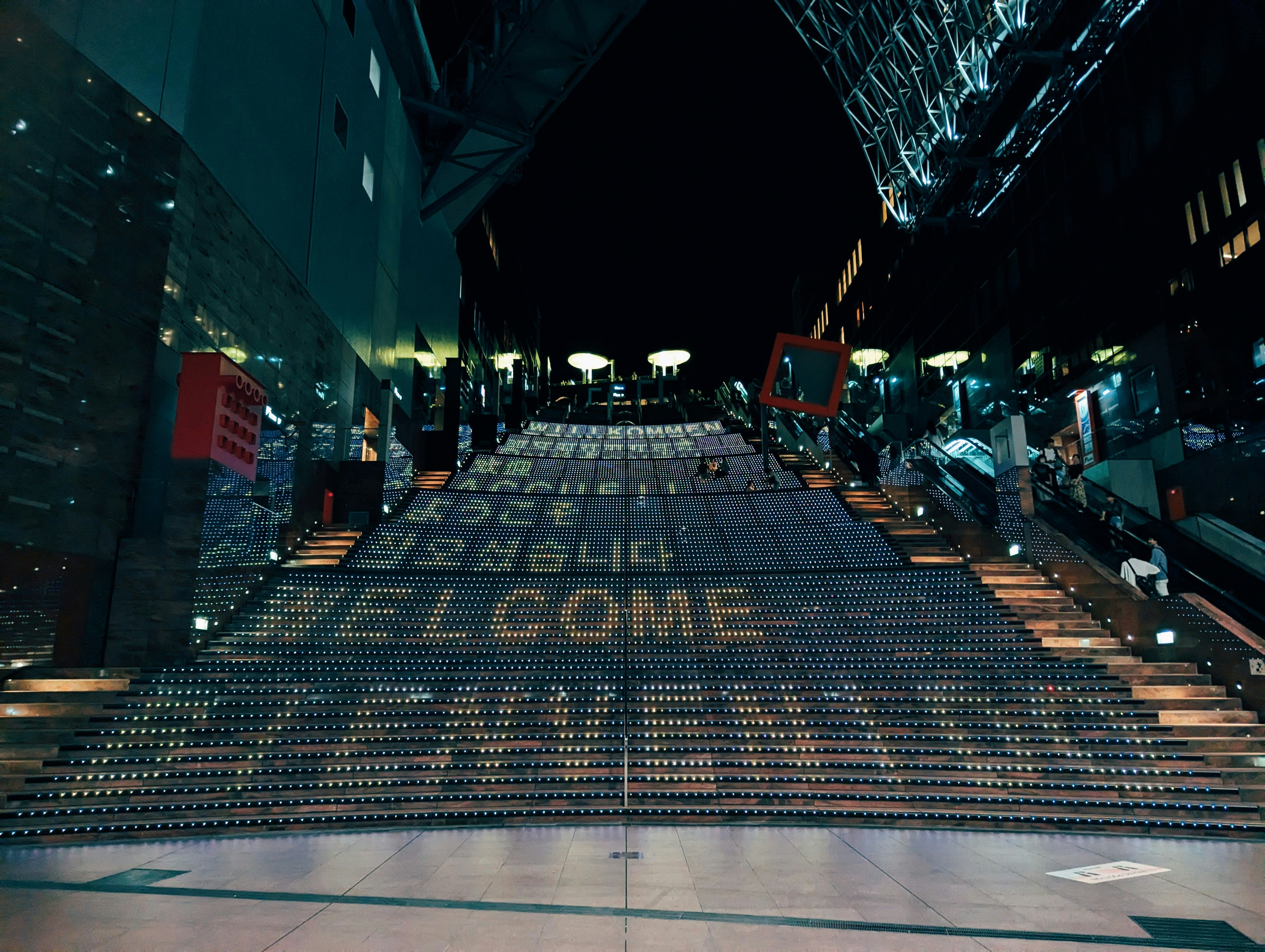 Et stort sett med trapper med ordene 'velkommen' skrevet på dem om natten. Dette bildet gir en følelse av invitasjon og varme, og oppfordrer leseren til å føle seg velkommen og engasjert i artikkelen.