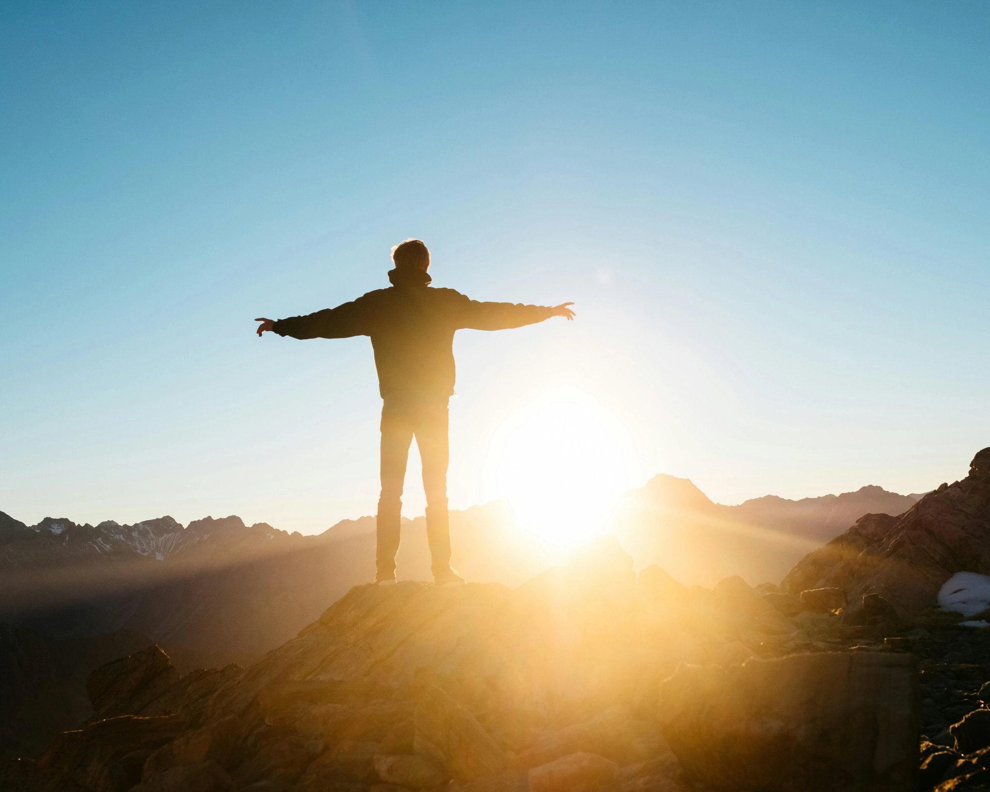 a man is standing on top of a mountain with his arms outstretched at sunset .