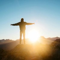 a man is standing on top of a mountain with his arms outstretched at sunset .
