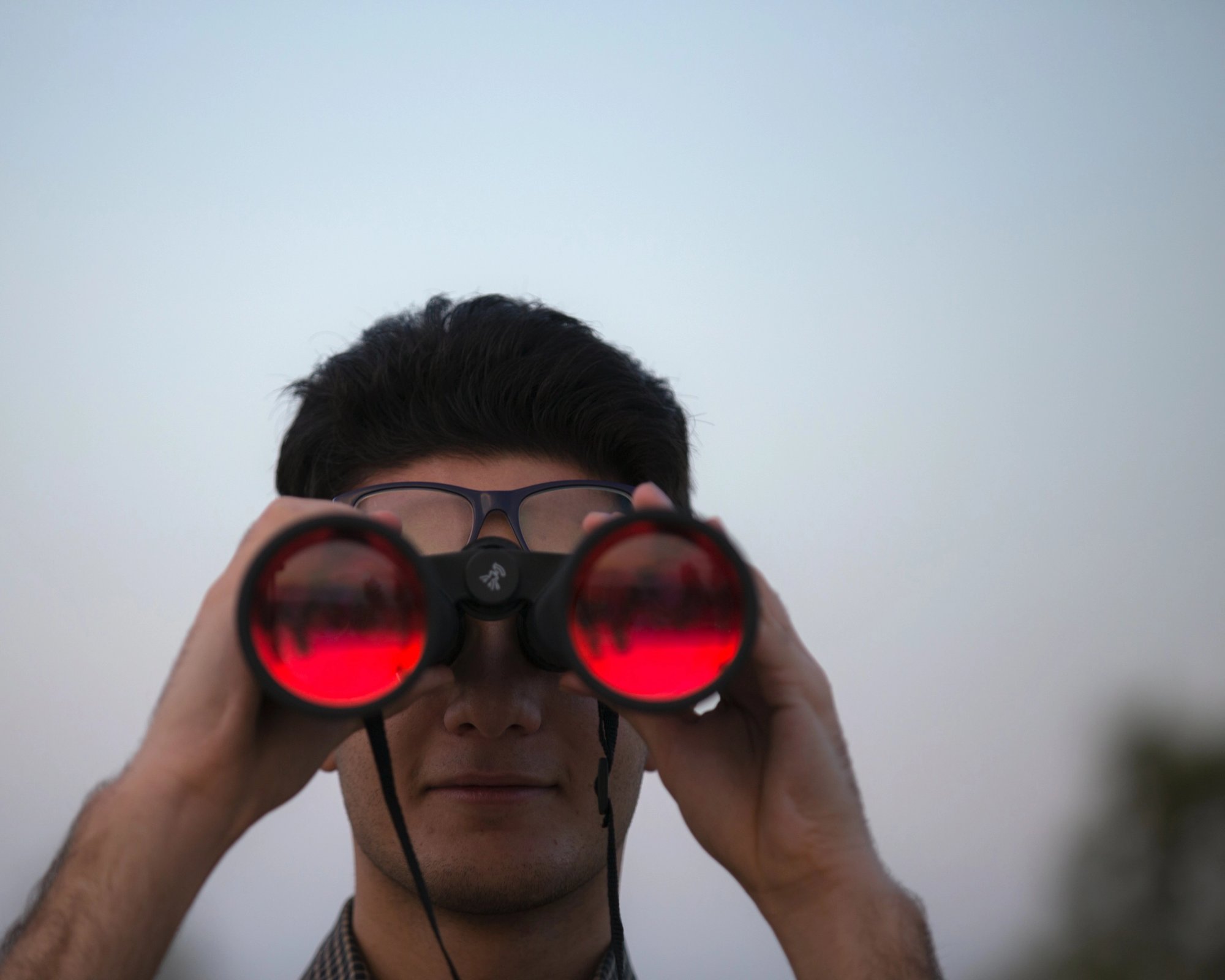 Person ser med kikkert på kameraet. Foto.