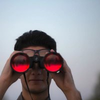 Person ser med kikkert på kameraet. Foto.