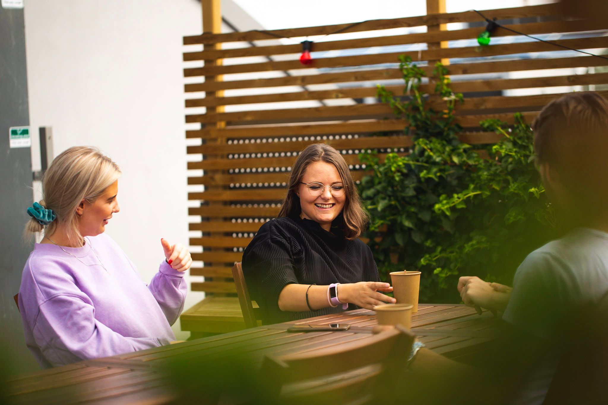 Caroline og Vilde i Kult Byrå sitter på et bord, drikker kaffe og prater