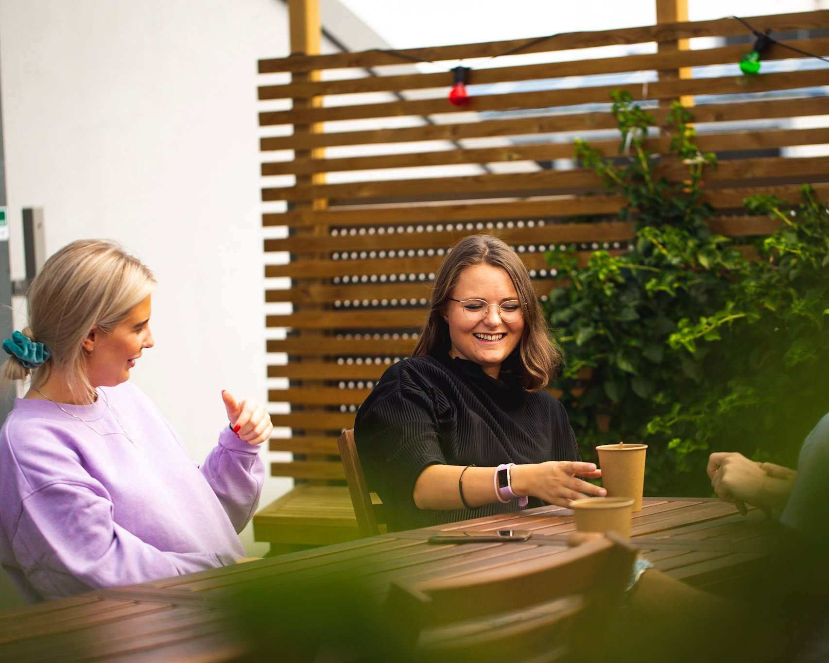 Caroline og Vilde i Kult Byrå sitter på et bord, drikker kaffe og prater