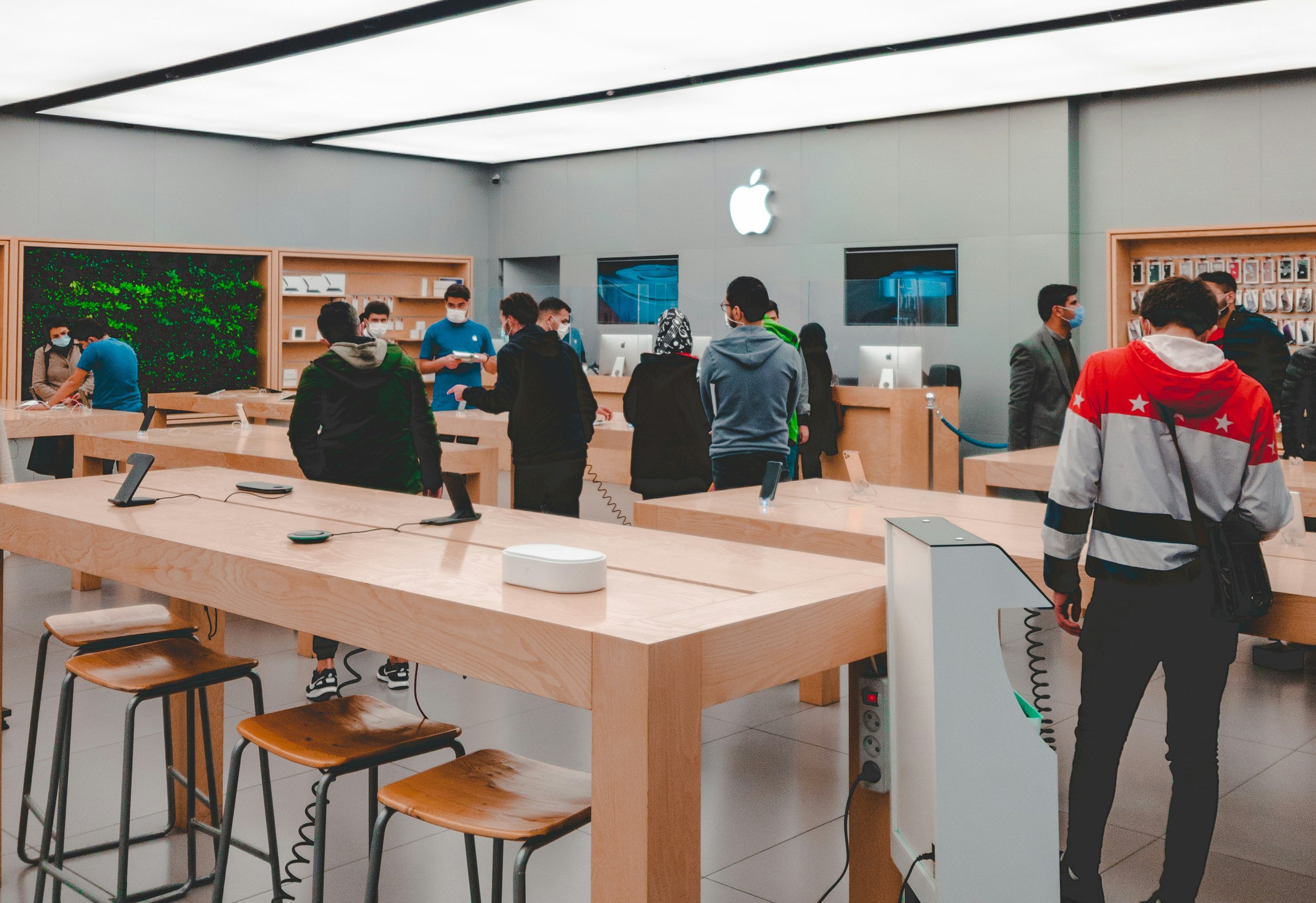 Inne i en Apple Store, der kunder går rundt og ser på produkter på trebord. Foto.